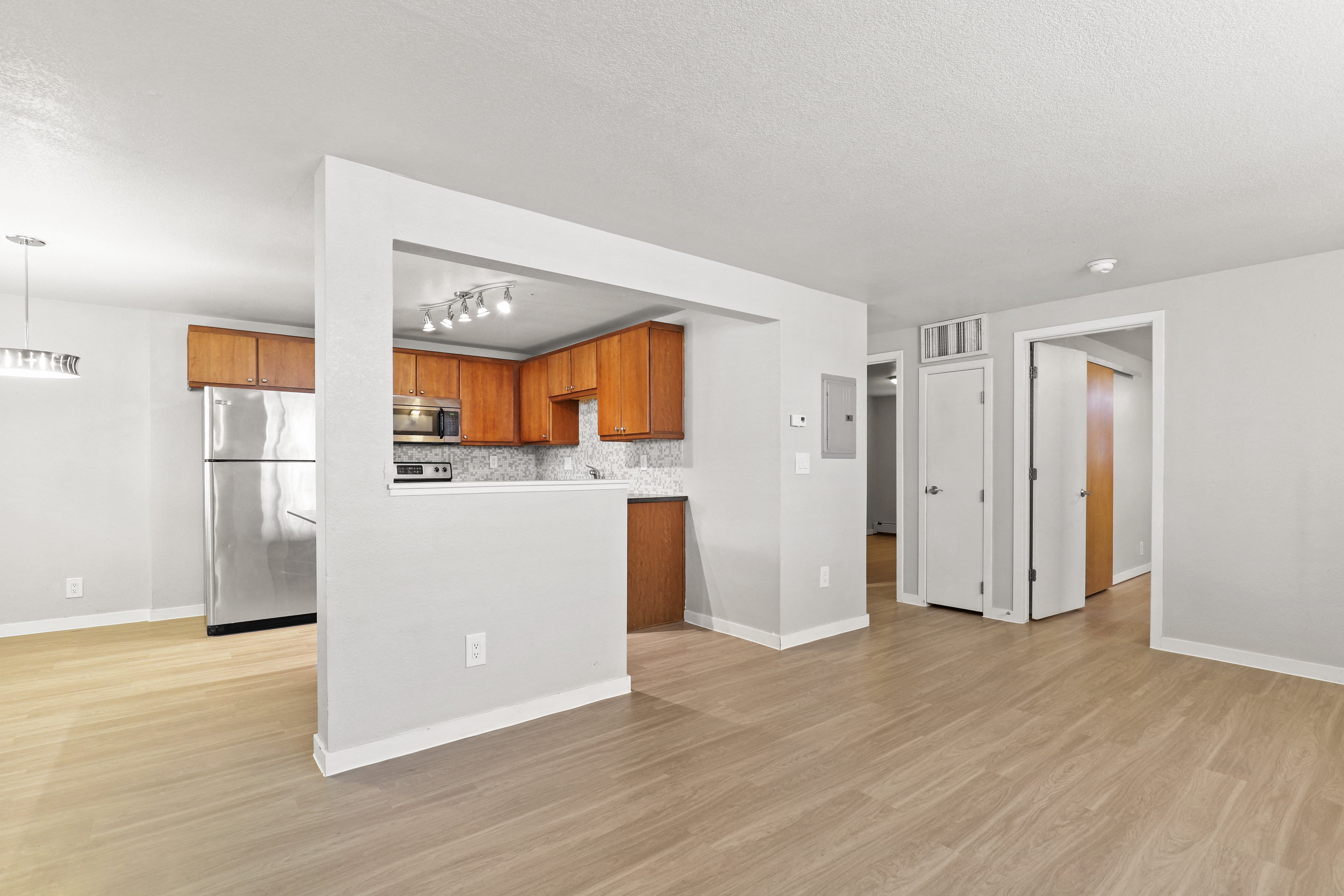 the living room and kitchen of an apartment with white walls and wood floors